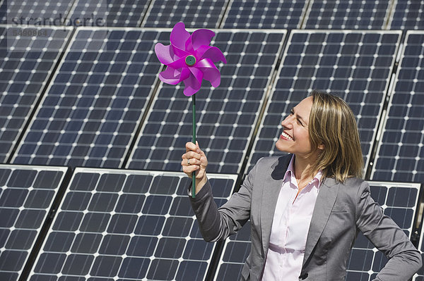Frau hält Papierwindmühle gegen Sonnenkollektoren  lächelnd