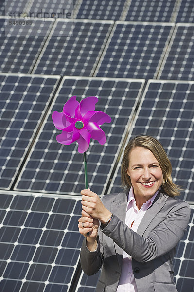 Frau hält Papierwindmühle gegen Sonnenkollektoren  lächelnd  Portrait