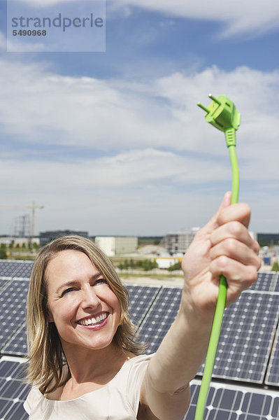Frau hält Stromkabel in Solarenergie  lächelnd