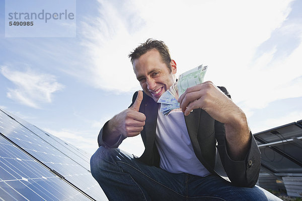 Mann mit Euro-Noten in Solaranlage  lächelnd  Portrait