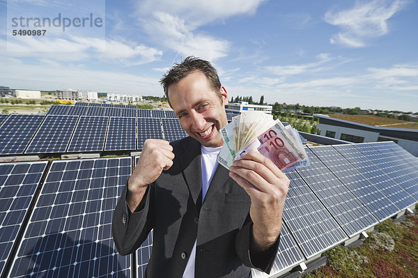 Mann mit Euro-Noten in Solaranlage  lächelnd  Portrait