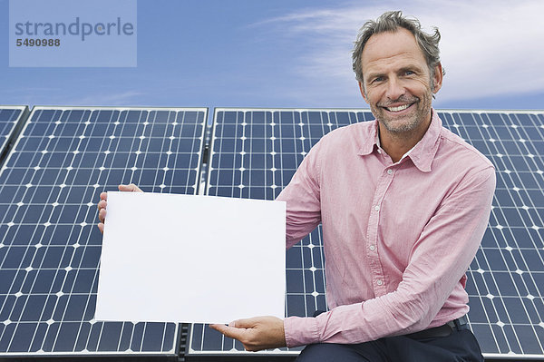 Älterer Mann hält weißes Brett in Solaranlage  lächelnd  Portrait