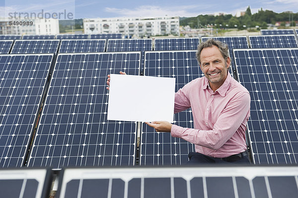 Älterer Mann hält weißes Brett in Solaranlage  lächelnd  Portrait