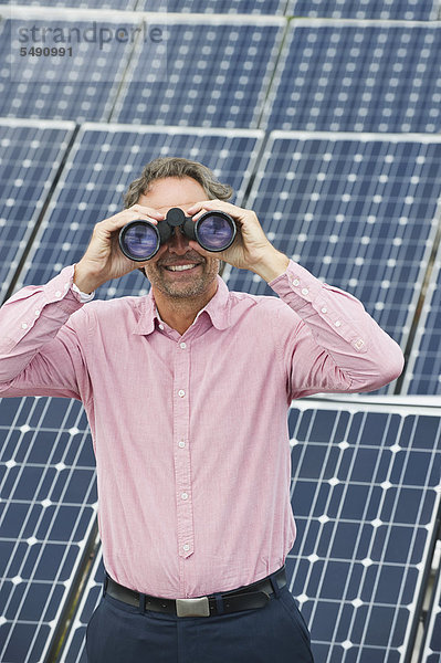Reifer Mann schaut durchs Fernglas in der Solaranlage  lächelnd