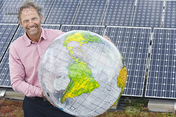 Erwachsener Mann hält Globus in Solaranlage  lächelnd  Portrait