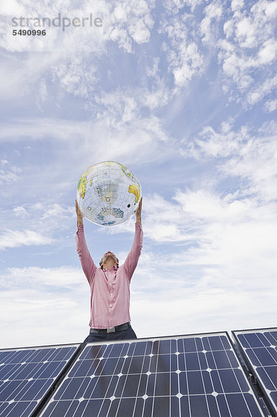 Erwachsener Mann hält Globus in Solaranlage