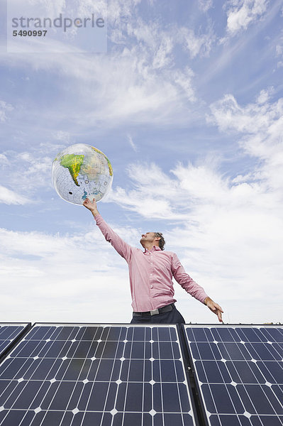 Reifer Mann balanciert Globus am Finger in Solaranlage