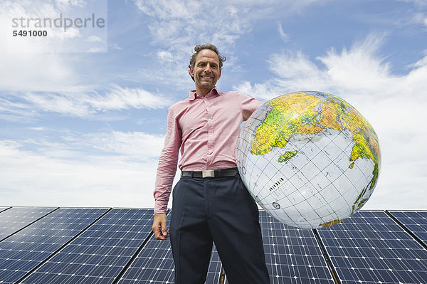 Erwachsener Mann hält Globus in Solaranlage  lächelnd  Portrait
