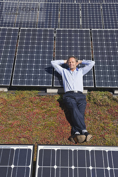 Reifer Mann  der sich auf einem Panel in einer Solaranlage ausruht  lächelnd
