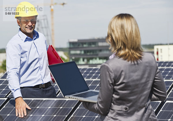 Deutschland  München  Ingenieure mit Laptop und Diskussion in Solaranlage