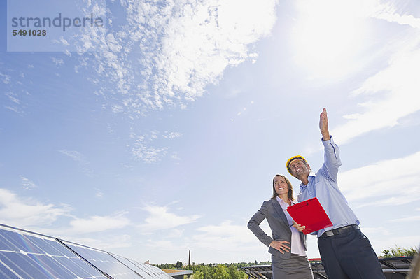 Deutschland  München  Ingenieure mit Klemmbrett in Solaranlage  lächelnd