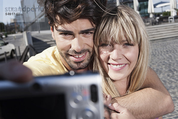 Deutschland  Köln  Junges Paar mit Handy zum Fotografieren  lächeln
