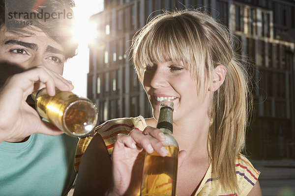 Deutschland  Köln  Junges Paar trinkt Bierflasche  lächelnd