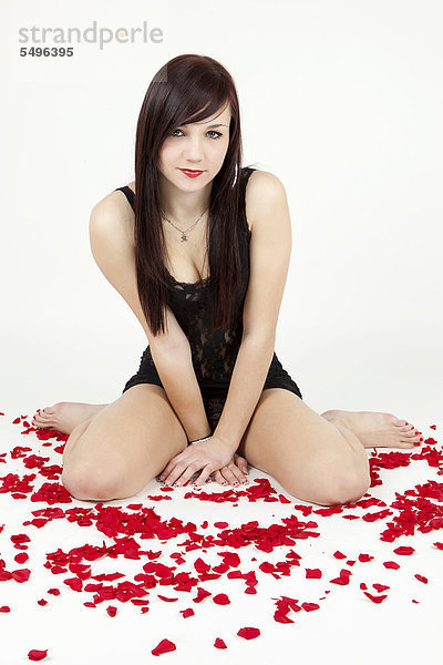 Junge Frau in schwarzen Dessous sitzt zwischen Rosenblättern