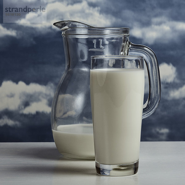 Milch in Kanne und Glas vor Wolkenhimmel