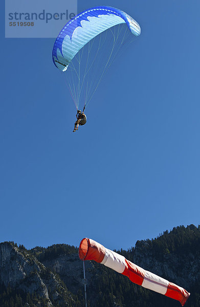 Gleitschirmflieger  Paraglider  beim Landeanflug gegen den Wind  vorne ein Windsack  hinten der Tegelberg  Oberbayern  Bayern  Deutschland  Europa  ÖffentlicherGrund