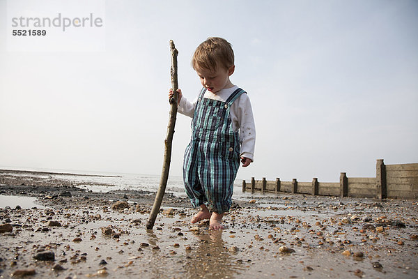 Kleinkind spielt mit Stock am Strand