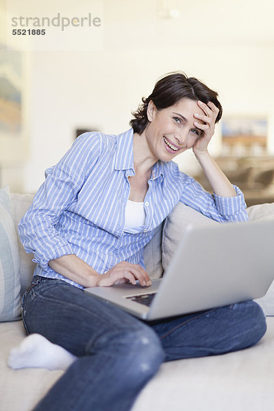 Lächelnde Frau mit Laptop auf der Couch