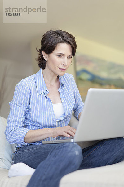 Lächelnde Frau mit Laptop auf der Couch