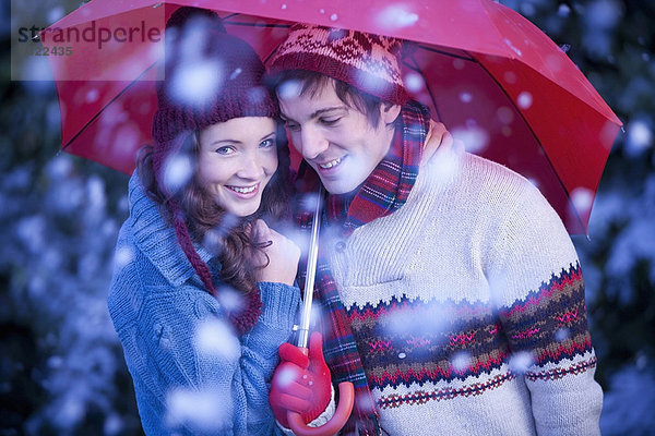 Lächelndes Paar unter dem Regenschirm im Schnee