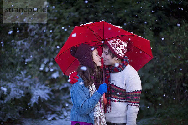 Lächelndes Paar unter dem Regenschirm im Schnee