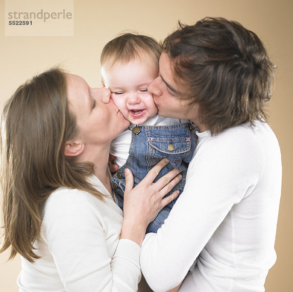 Eltern küssen lächelndes Kleinkind