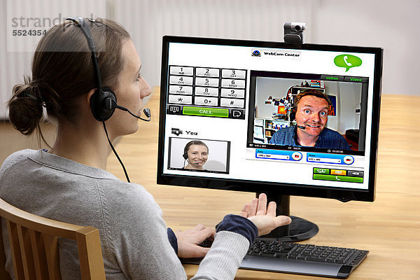 Junge Frau sitzt am Computer und telefoniert über das Internet  per Webcam wird das Livebild beider Teilnehmer übertragen