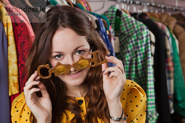 Junge Frau versucht auf Spaßbrille in Kleidung Shop  Lächeln