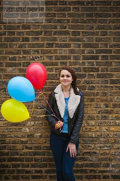 Young Woman holding bunten Luftballons gegen Wand