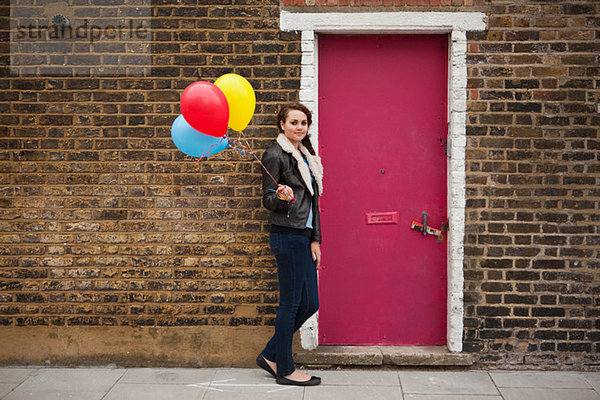 Young Woman holding bunten Luftballons gegen Wand