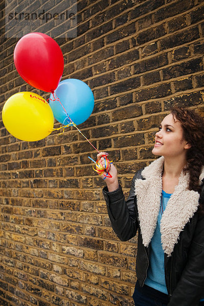 Young Woman holding bunten Luftballons gegen Wand