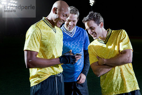 Fußballspieler beim Blick auf das Handy auf dem Spielfeld