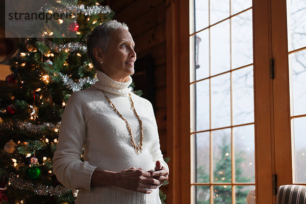 Reife Frau stehend von Weihnachtsbaum  Blick durchs Fenster
