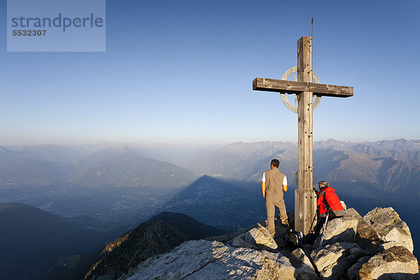 Bergsteiger bei Sonnenaufgang am Gipfelkreuz des Ifingers oberhalb von Meran  Meran 2000  Südtirol  Italien  Europa