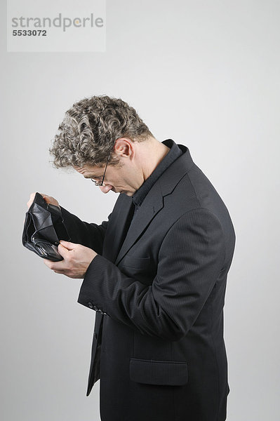 Geschäftsmann in schwarzem Anzug schaut in seine leere Geldbörse