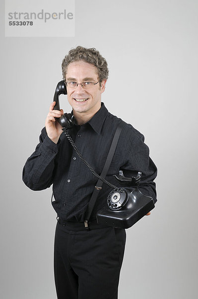 Geschäftsmann in schwarzem Anzug mit historischem Telefon W 38