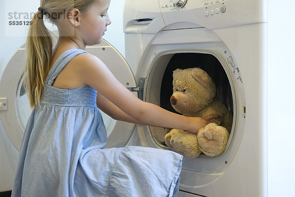 Kleines Mädchen nimmt Teddybär aus dem Trockner