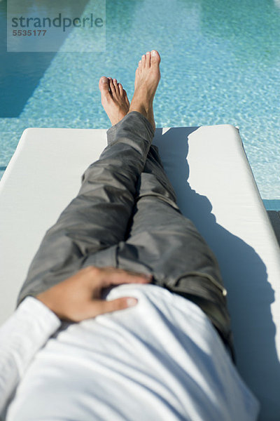 Mann entspannt sich auf Liegestuhl neben dem Pool