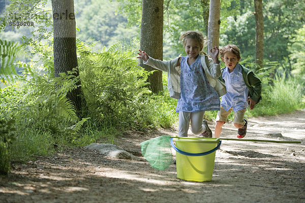 Kinder laufen auf Eimer und Schmetterlingsnetz im Wald zu.