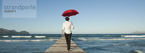 Mann auf Pier mit Regenschirm  Rückansicht