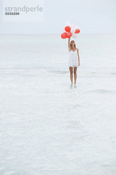 Frau steht auf der Wasseroberfläche und hält einen Haufen Luftballons.