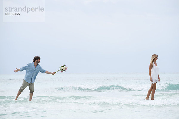 Ein Paar steht im Meer  eine Frau geht vom Mann weg  während er einen Strauß ausstreckt.