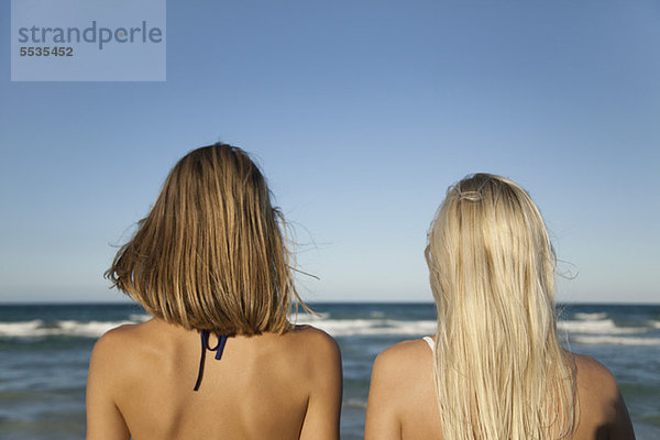 Frauen Seite an Seite am Strand  Blick aufs Meer  Rückansicht