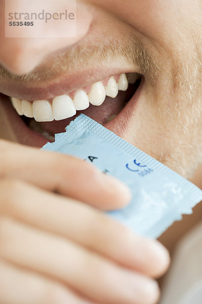 Mann öffnet Kondomhülle mit den Zähnen  abgeschnitten