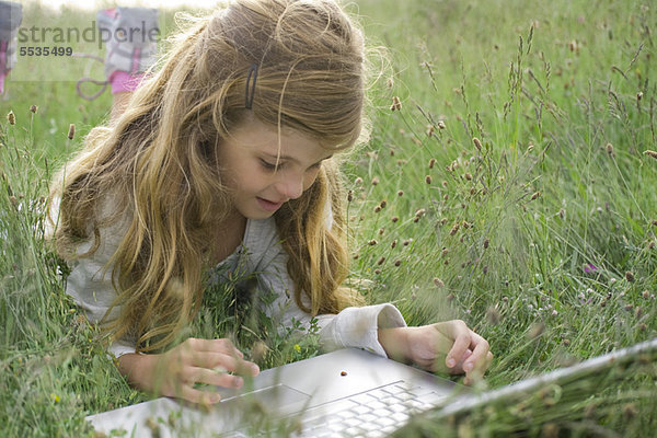 Mädchen im Gras liegend  Marienkäfer beim Krabbeln am Laptop beobachtend