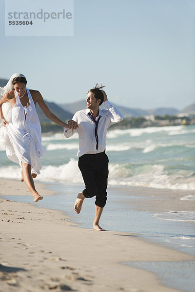 Braut und Bräutigam laufen Hand in Hand am Strand.