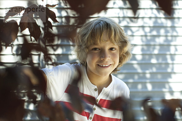Junge lächelt hinter Baumästen