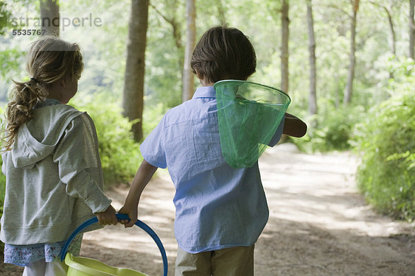 Kinder beim Waldspaziergang mit Schmetterlingsnetz und Eimer