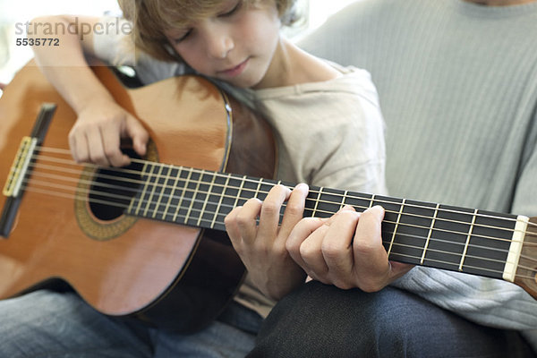 Junge lernt mit Vater Gitarre spielen