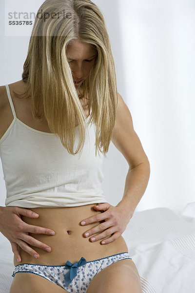 Frau sitzt auf dem Bett und schaut auf den Bauch.